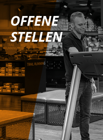 Ein Mann steht neben einem Laufband in einem Geschäft, im Hintergrund sind Kartons zu sehen. Der Text auf dem Bild lautet „OFFENE STELLEN“ und weist auf offene Stellen hin. Die linke Seite des Bildes ist orangefarben.