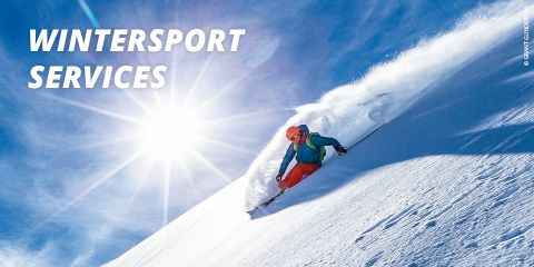 Ein Skifahrer in roter Hose und blauer Jacke fährt unter strahlend blauem Himmel einen schneebedeckten Hang hinunter. Die Sonne scheint hell und beleuchtet den Schnee. In der oberen linken Ecke steht „Winter Sport Services“.